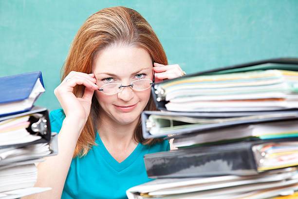 Teacher or Graduate Student Holding Glasses With Piles of Work.